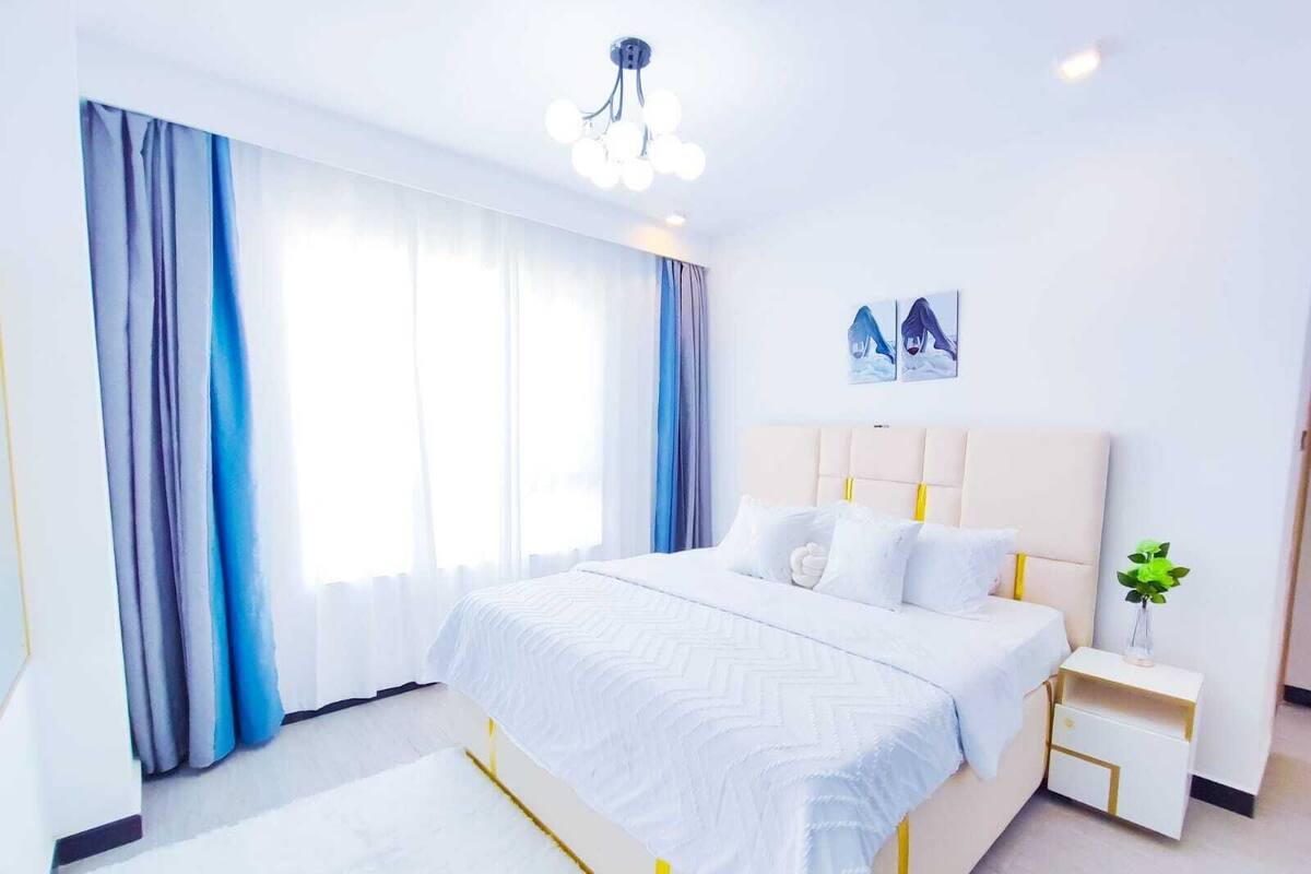 Una habitación de hotel moderna con una cama grande, una mesita de noche con lámpara y una ventana con cortinas.