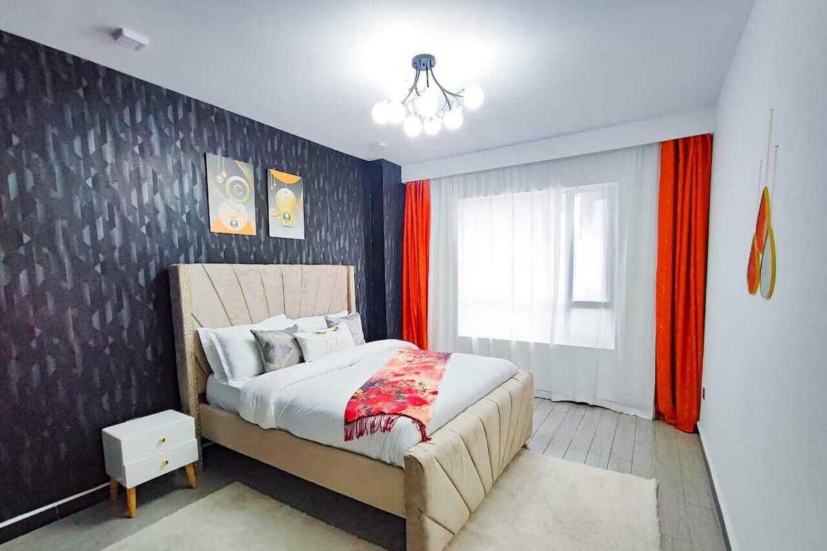 Un dormitorio moderno con cama, mesita de noche y un gran ventanal con cortinas.