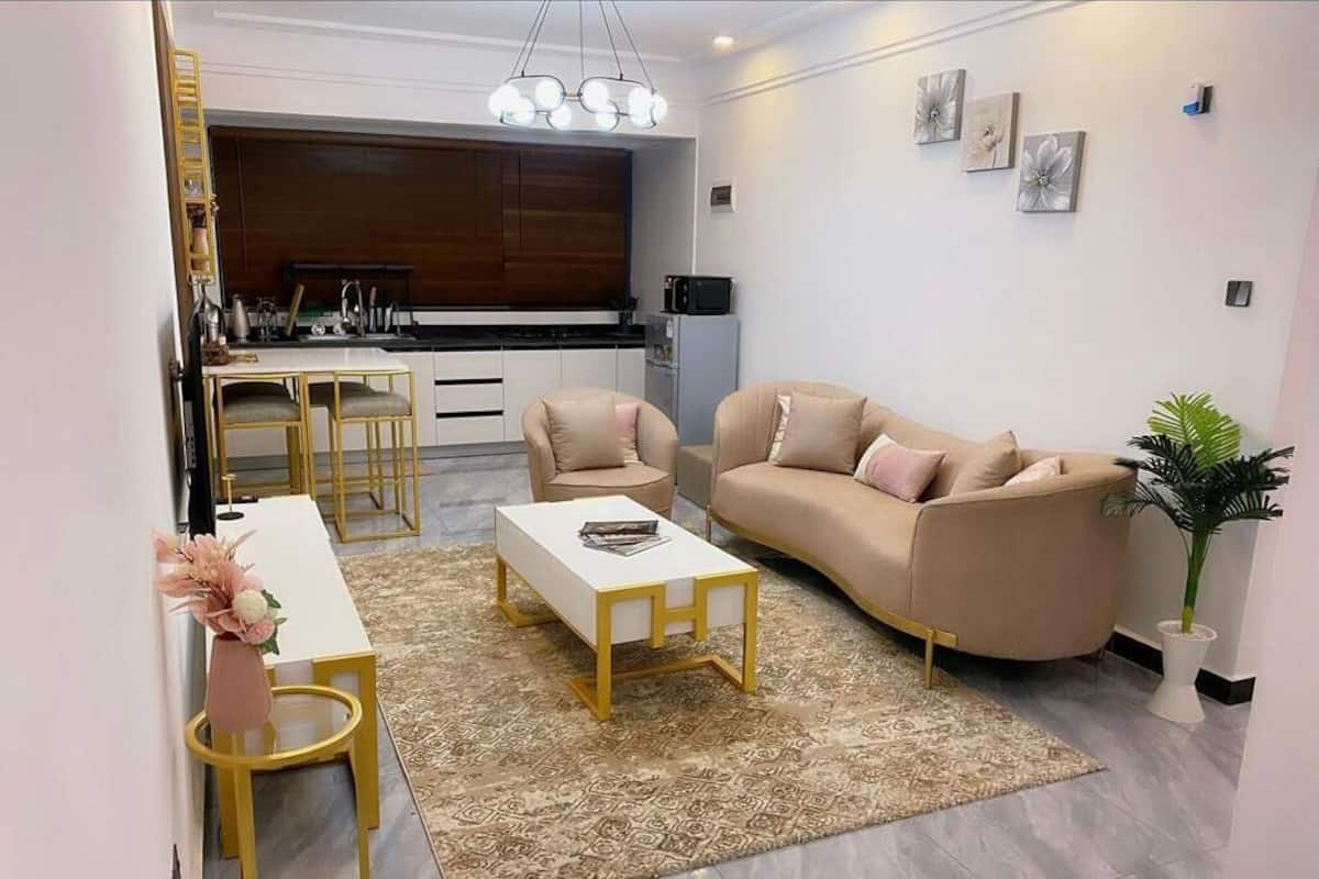 Una sala de estar moderna con sofá, mesa de centro y comedor con mesa blanca y sillas doradas.