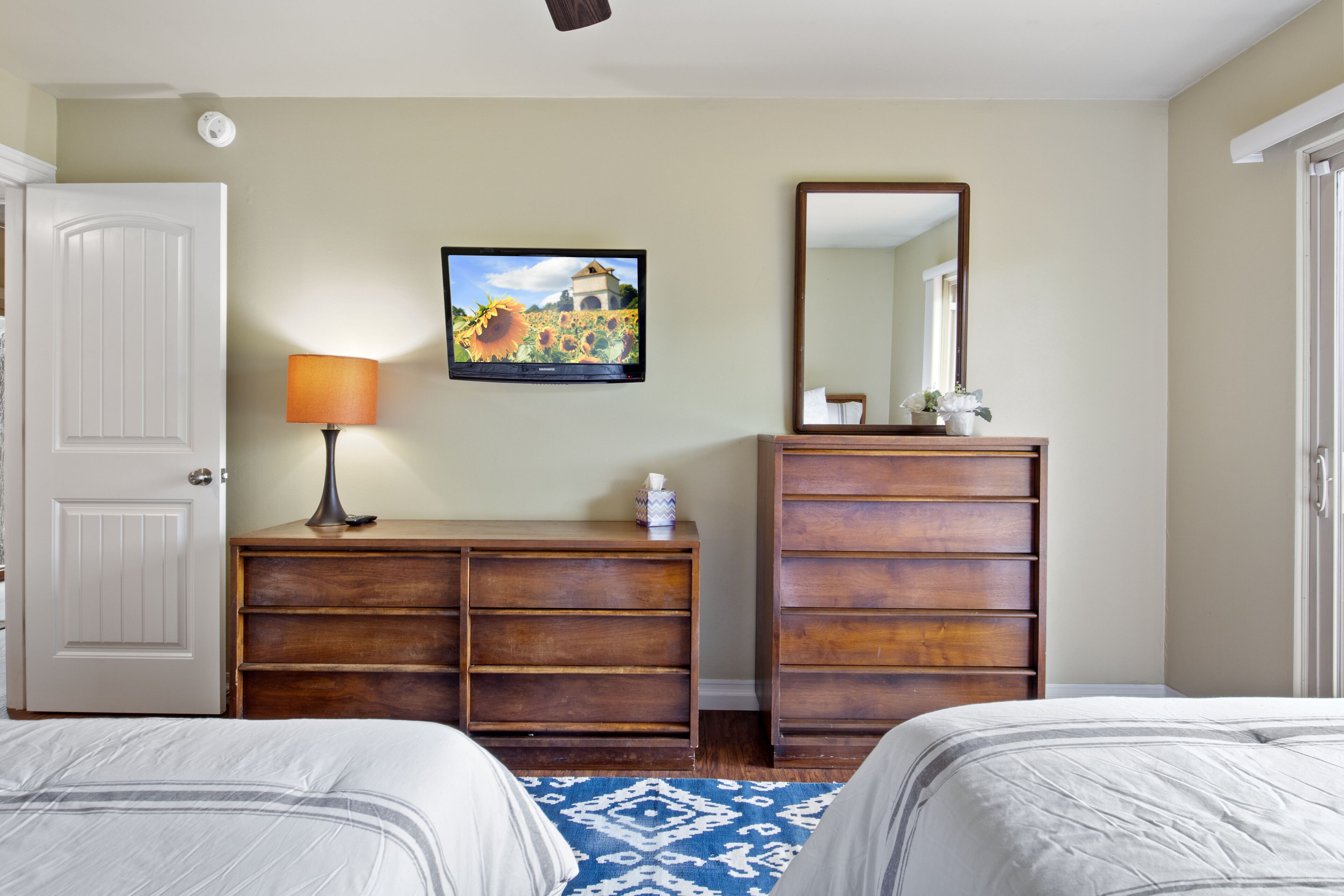 A hotel room with two beds, a wooden dresser, a mirror, a television, and a patterned rug.