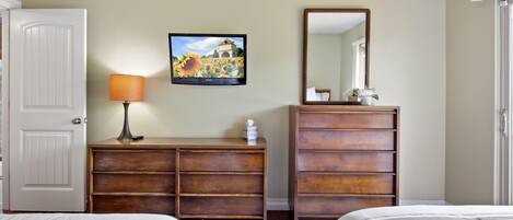 A hotel room with two beds, a wooden dresser, a mirror, a television, and a patterned rug.