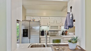Une cuisine moderne avec des meubles blancs, des appareils en acier inoxydable et un plateau en bois sur lequel est posée une plante.