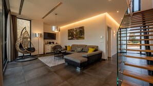 A modern living room with a sectional sofa, a hanging chair, and a staircase.