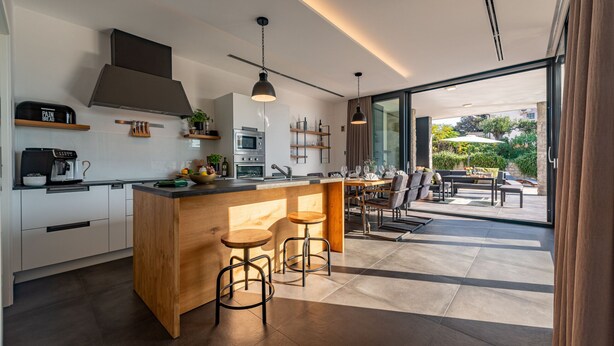 A modern kitchen with a central island, bar stools, and a dining area with outdoor seating.