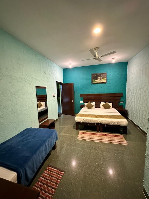 A bedroom with two single beds, a large bed, a ceiling fan, and a painting on the wall.