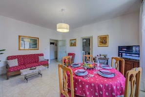 Un coin repas avec une table dressée pour quatre personnes, un canapé et un téléviseur.
