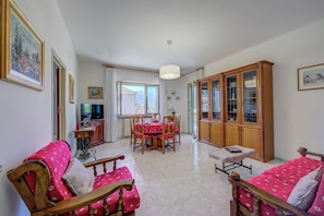 A living room with a dining area, wooden furniture, and a view through the window.