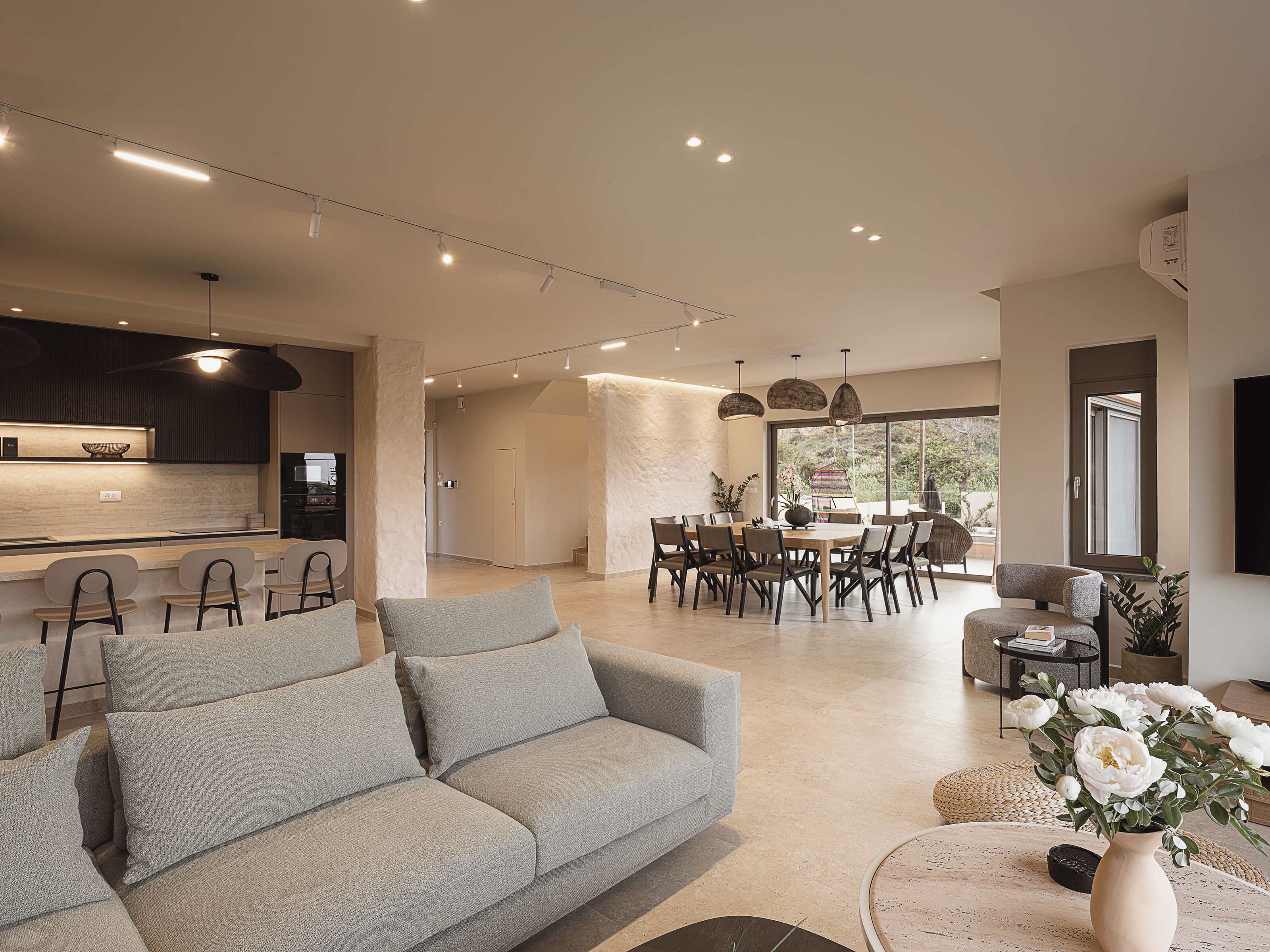 Ein modernes Wohnzimmer mit einem grauen Sofa, einer Essecke mit Tisch und Stühlen sowie einer Küche im Hintergrund.