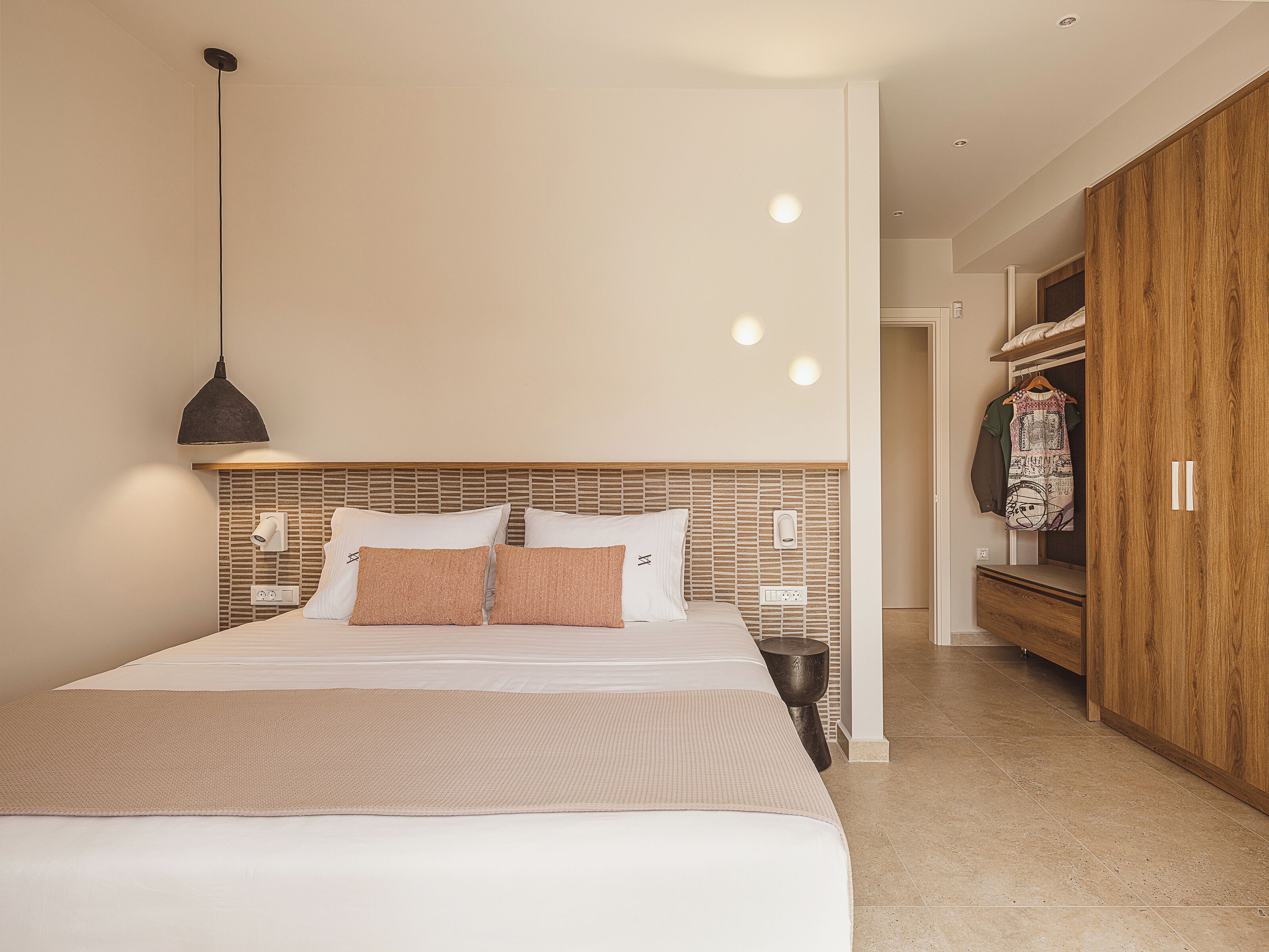 Ein modernes Schlafzimmer mit einem großen Bett, einem Holz-Kopfstück, einer hängenden Pendelleuchte und einem Kleiderschrank.