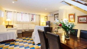 A hotel room with a checkered floor, a dining table with chairs, a sofa, a TV, and a window with curtains. - Casa en Pleno Centro (Sevilla)