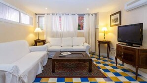 A living room with a white sofa, a coffee table, a TV, and a patterned rug. - Casa en Pleno Centro (Sevilla)