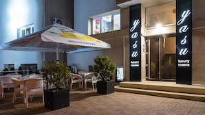 A hotel entrance with 'Yaa luxury rooms' signage, outdoor seating, and a 'Fresh 0.0 mix de suc si bere' umbrella. - Yasu Luxury Rooms (Bucharest)