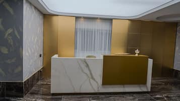 Un área de recepción con un mostrador de mármol, un ventanal con cortinas translúcidas y una pared decorada con detalles dorados.