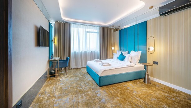 A modern hotel room with a large bed, a desk, and a TV. - Yasu Luxury Rooms (Bucharest)