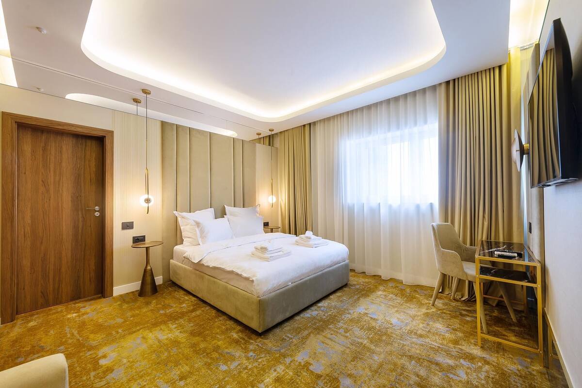 A hotel room with a large bed, a desk with a chair, a TV, and a window with curtains.