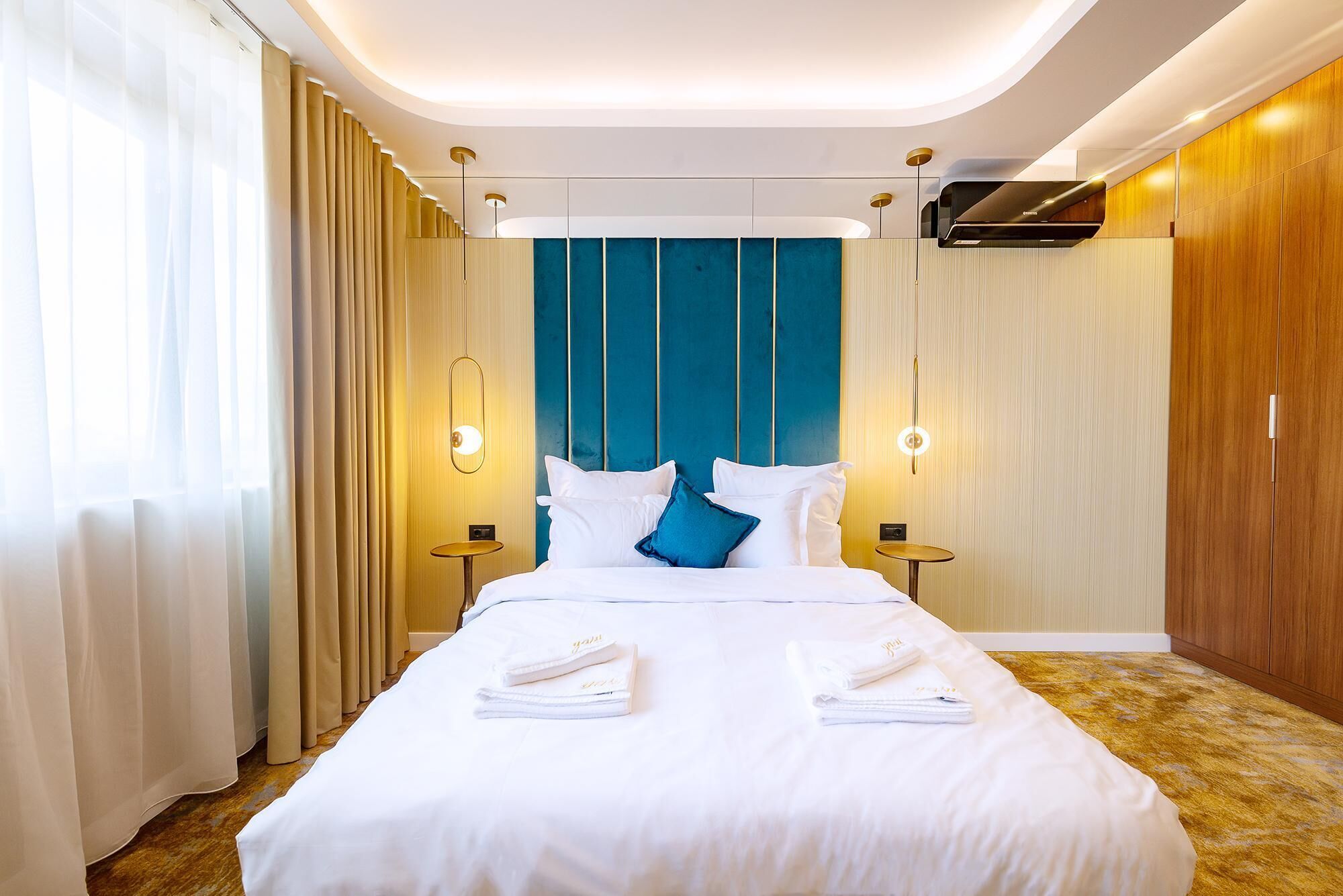 Una habitación de hotel moderna con una cama grande, dos mesitas de noche, un armario empotrado y una lámpara en el techo.
