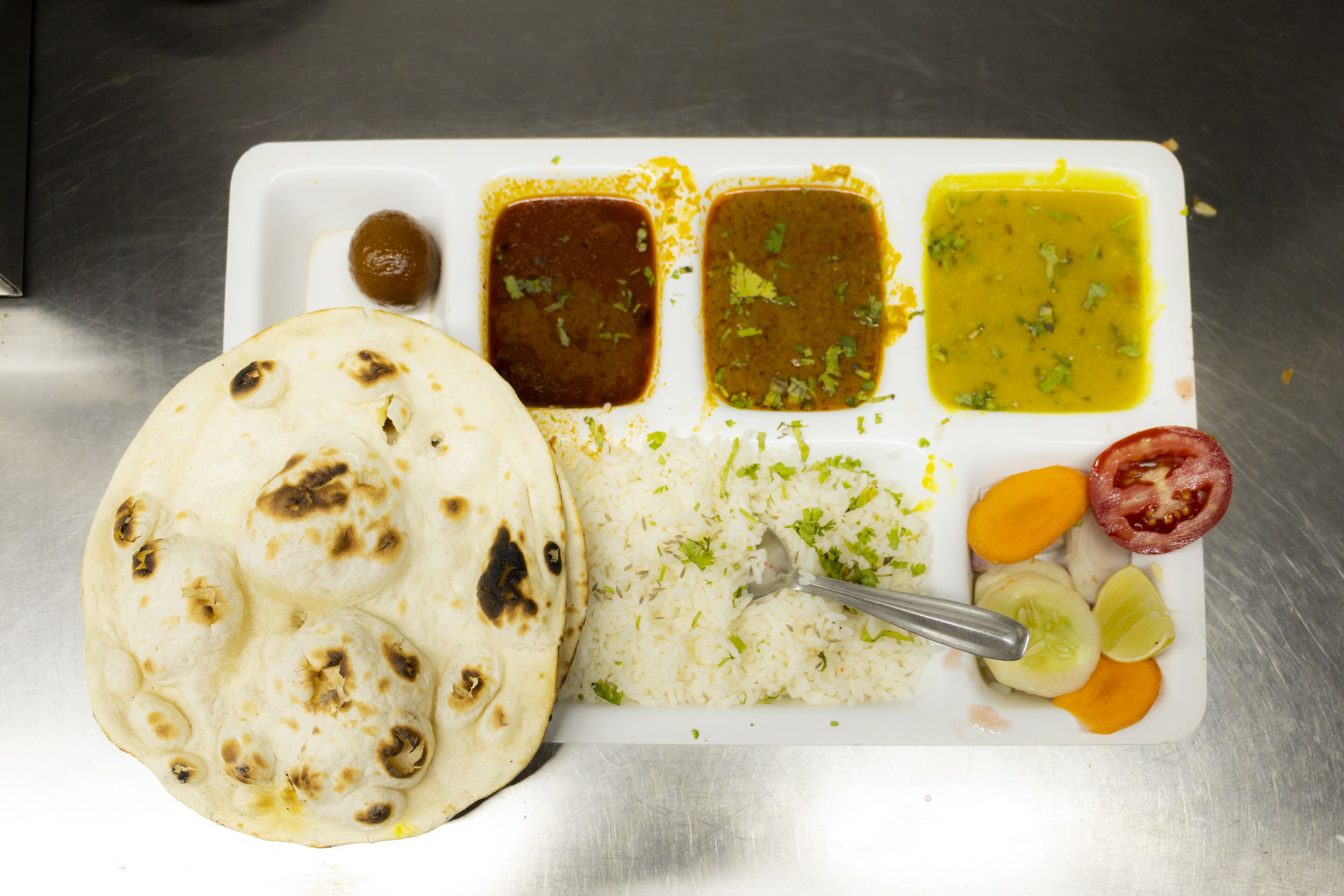 A meal with rice, flatbread, and various sauces on a white plate.