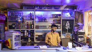 Un bar con un refrigerador lleno de bebidas, una barra con una computadora y un letrero de neón.