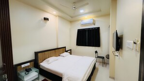 Habitación de hotel con cama, escritorio, silla, televisor, aire acondicionado y ventilador de techo.