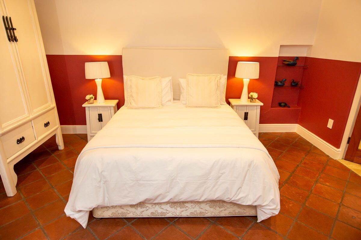 A neatly arranged bedroom with a large bed, two bedside tables with lamps, and a red accent wall.