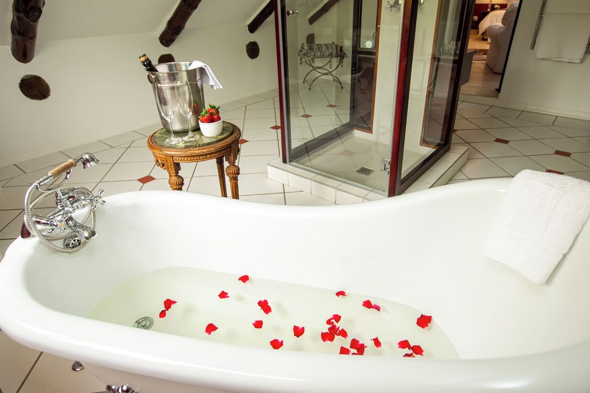 Une salle de bain avec une baignoire sur pieds, une douche à parois de verre et une petite table sur laquelle se trouvent une bouteille et des verres.