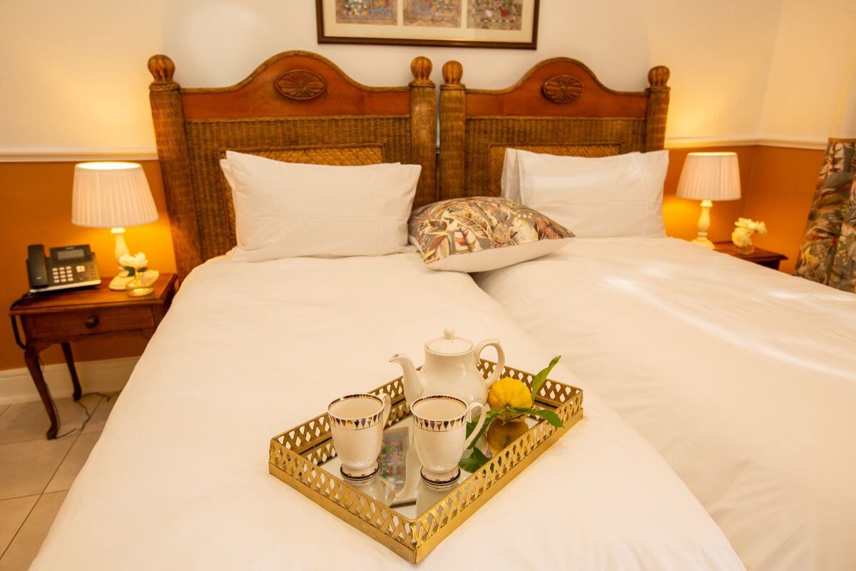 Habitación de hotel con una cama grande, dos mesitas de noche, un teléfono y una bandeja con tazas de té y una tetera.