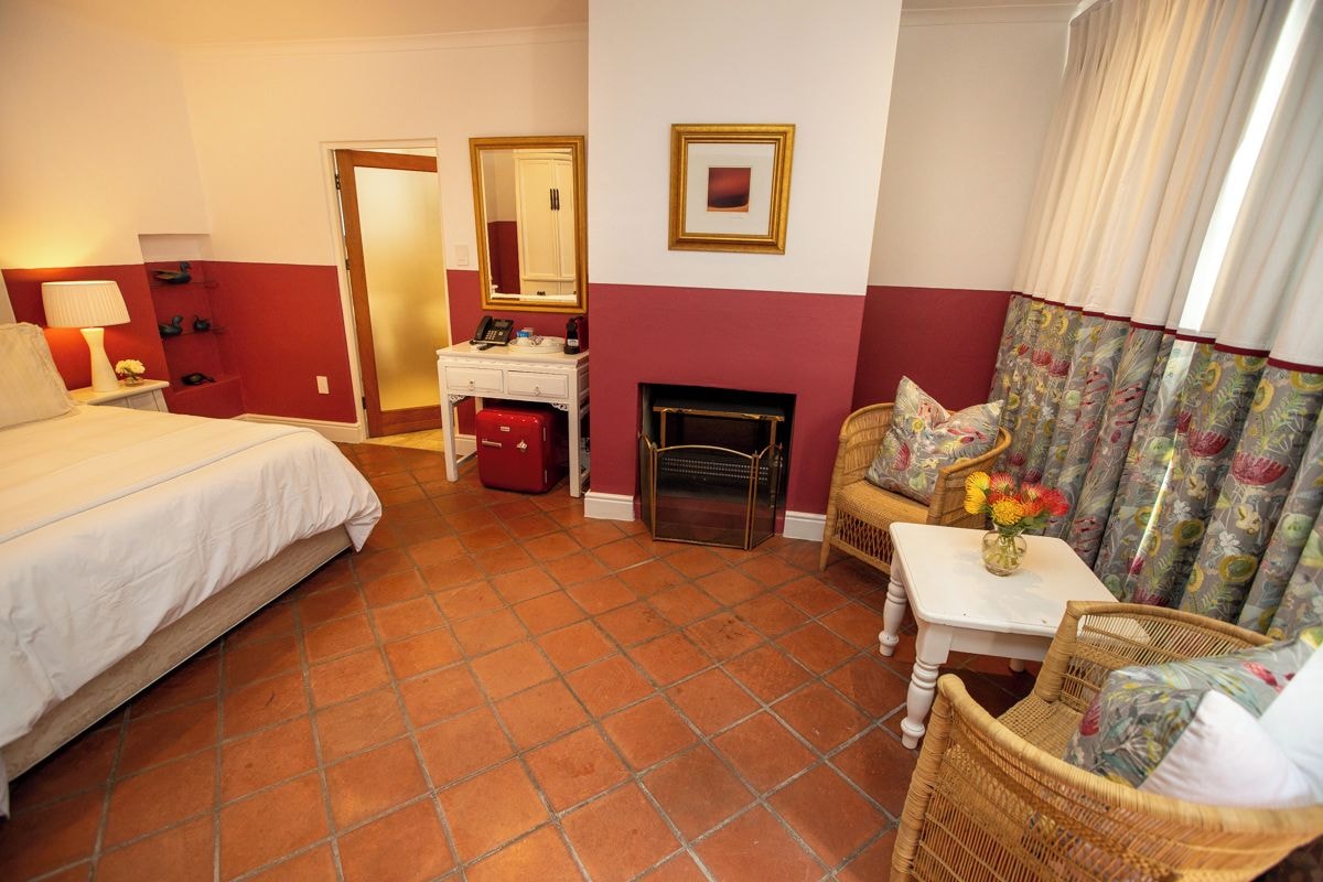 Une chambre d’hôtel avec un lit, une petite table sur laquelle est posé un vase, une cheminée et un fauteuil en osier.