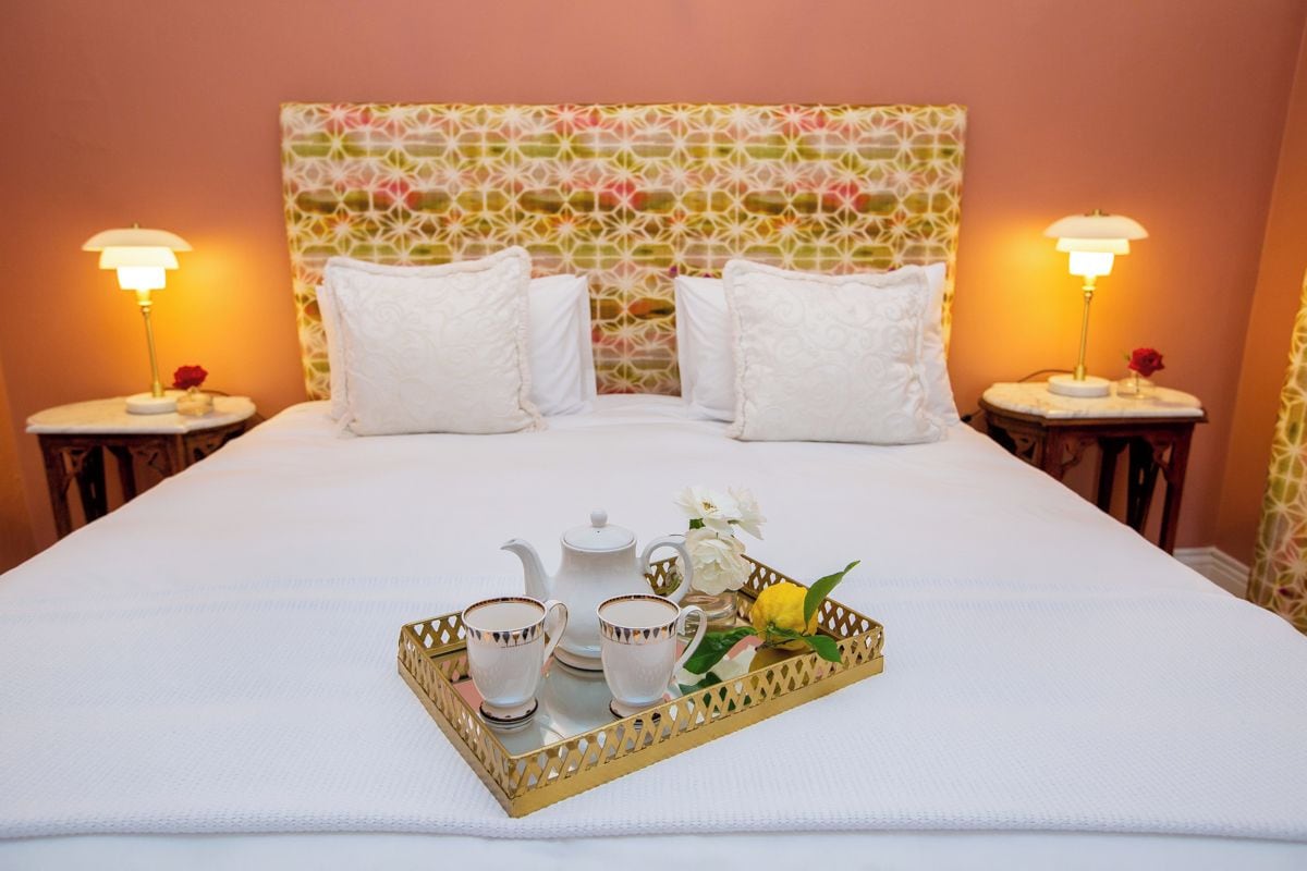 Un lit bien fait, agrémenté d’un plateau avec des tasses à thé, une théière et des fleurs, le tout placé devant une tête de lit à motifs.
