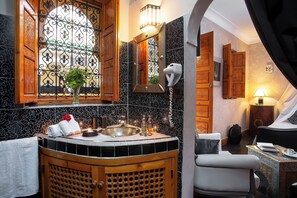 A bathroom with a wooden vanity, a sink, and a mirror. There is a towel and a vase with flowers on the vanity. - Riad Rodaina & Spa (Marrakech)