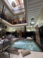 Una piscina cubierta de varios niveles con techo de cristal, un área de descanso con asientos y una fuente decorativa.