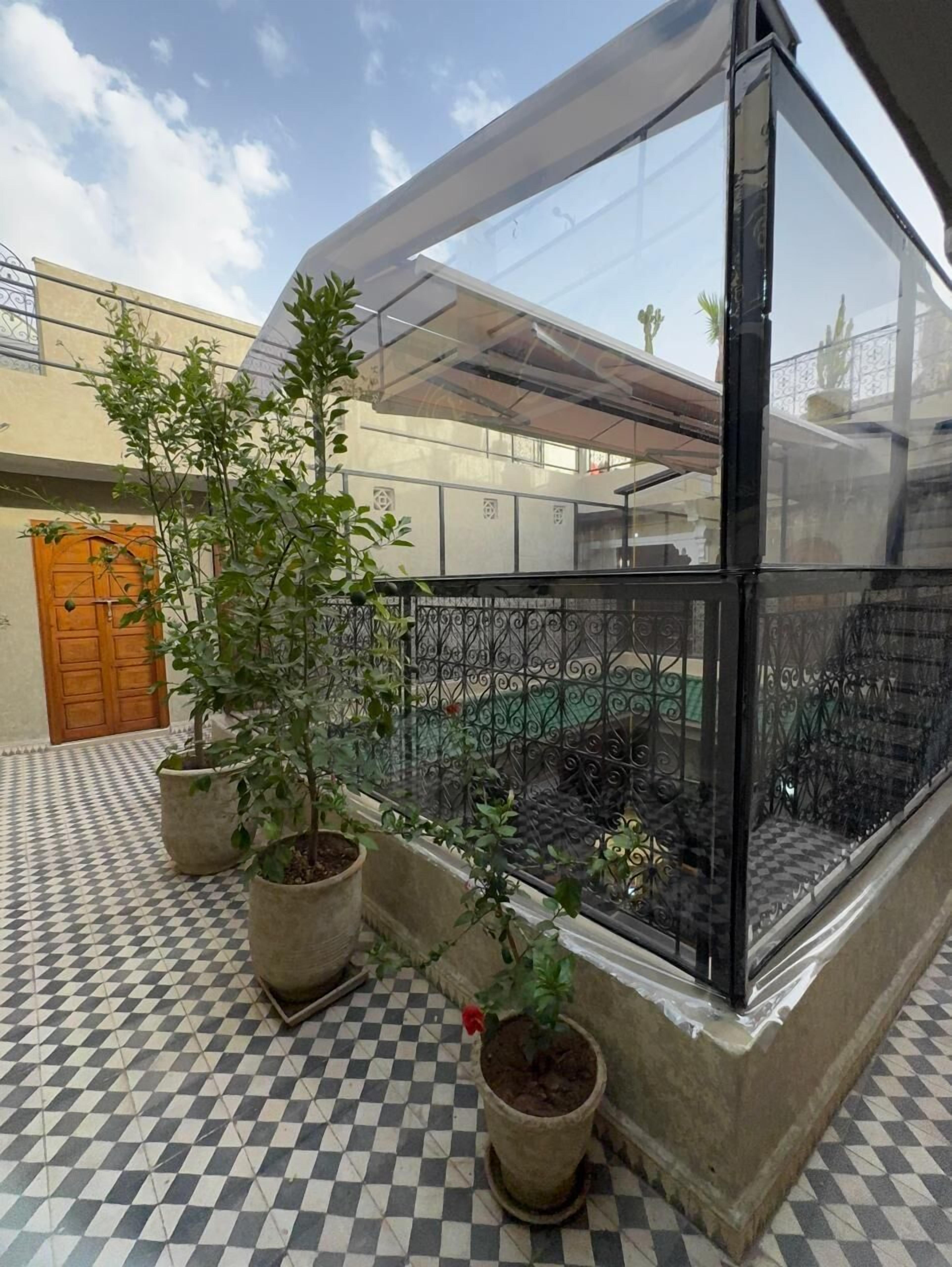 A glass-enclosed balcony with potted plants, a checkered floor, and a wooden door.