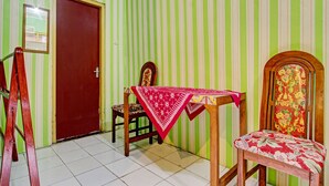Una habitación con pared verde y blanca a rayas, una puerta de madera, una mesa con mantel rojo, una silla de madera con cojín floral y un banco de madera.