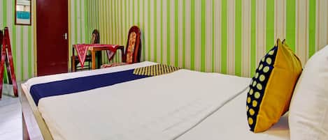 A hotel room with a bed, a small table with a red tablecloth, two chairs, a red door, and green and white striped walls.