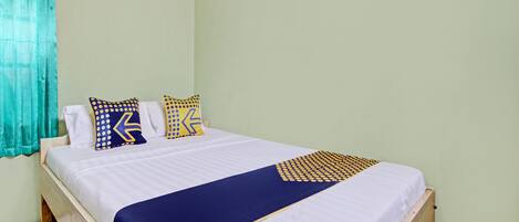 A single bed with a white and blue bedspread, two decorative pillows, and a blue accent pillow.
