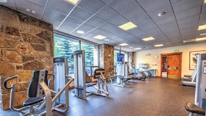 A gym with various exercise machines, stone walls, and large windows. - Hyatt Residence Club - Main Street Station 2 Bedroom (Breckenridge)