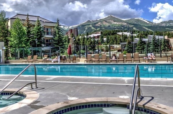 A pool area with lounge chairs and a hot tub, surrounded by buildings and mountains. - Hyatt Residence Club - Main Street Station 2 Bedroom (Breckenridge)