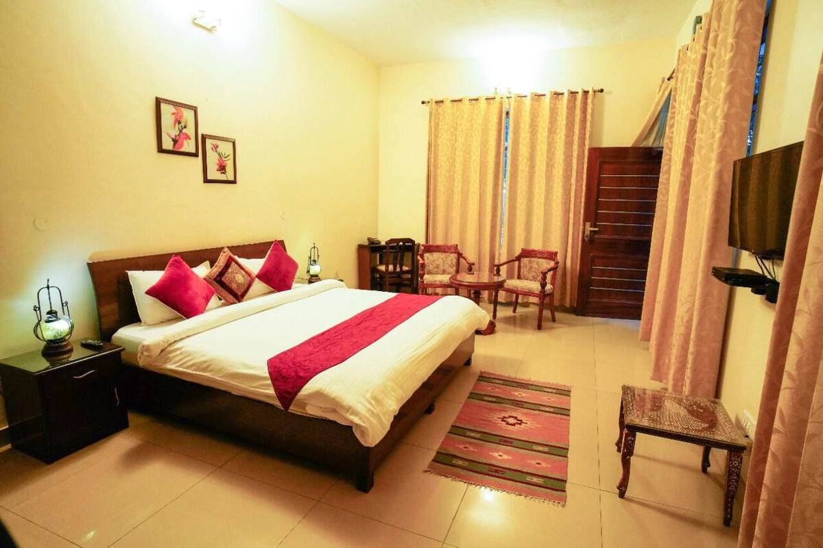 A hotel room with a bed, nightstands, a TV, a desk, and a chair.