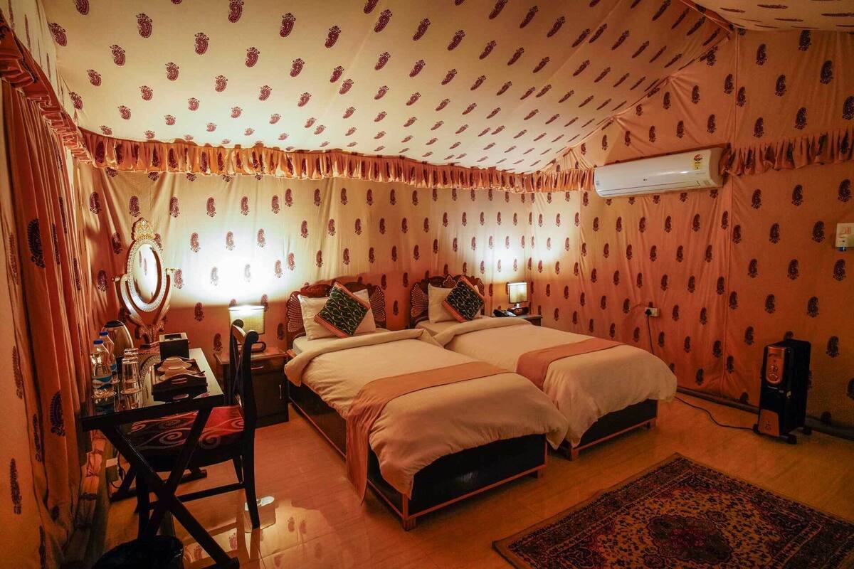 A room with two beds, a desk with a chair, a mirror, and an air conditioning unit.