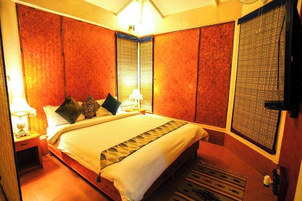 A hotel room with a large bed, two bedside tables with lamps, a decorative wall panel, and a window with a patterned blind.