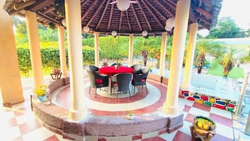 A covered outdoor dining area with a circular table and chairs, surrounded by a checkered floor and a decorative border.