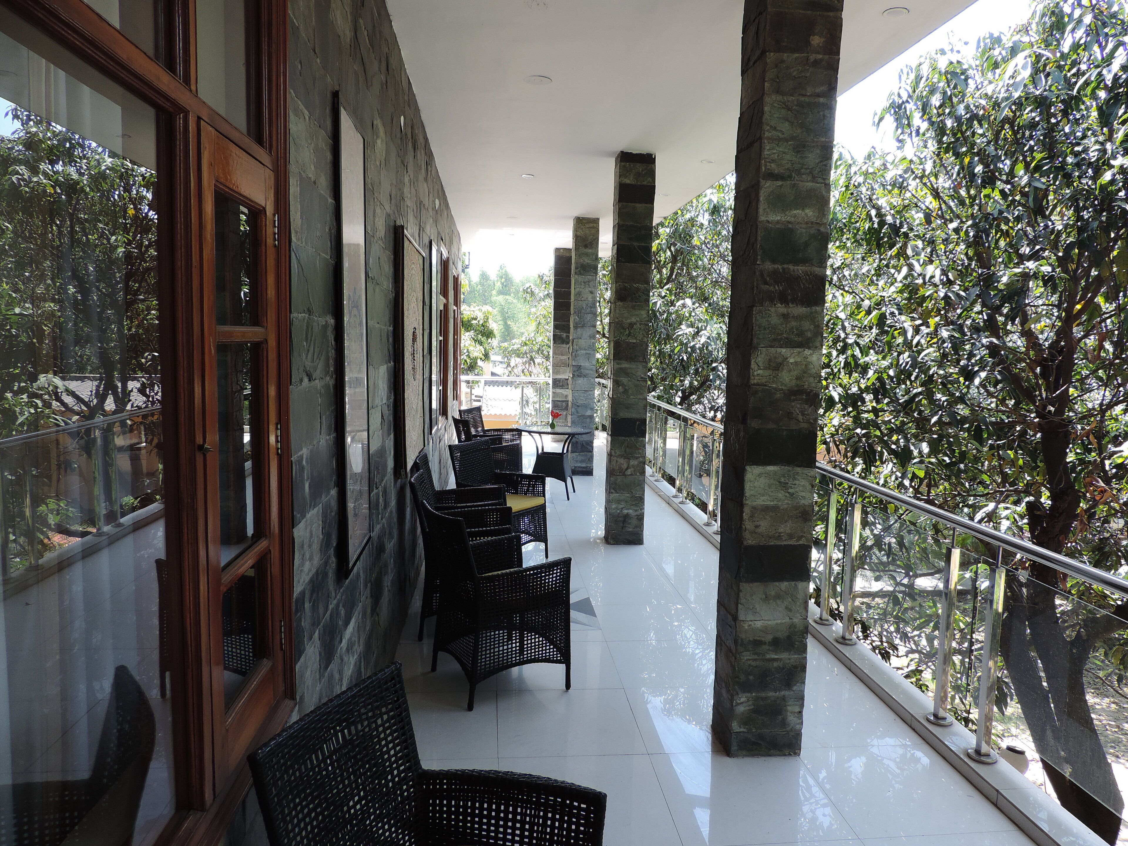 A covered outdoor seating area with stone pillars, wicker furniture, and a view of greenery.