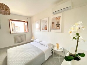 A hotel room with a bed, a small table, a chair, a radiator, a window, and a wall-mounted air conditioner. - Casa Edoardo Two Bedroom Pizzo Calabro (Pizzo)