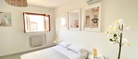 A hotel room with a bed, a bedside table, a lamp, a potted orchid, and framed pictures on the wall.