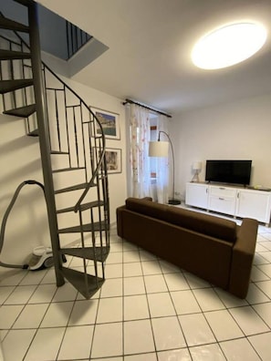 A living room with a spiral staircase, a brown sofa, a television, and a cabinet. - Casa Edoardo Two Bedroom Pizzo Calabro (Pizzo)