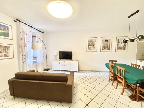 A living room with a sofa, a dining table with chairs, a TV on a cabinet, and framed pictures on the wall. - Casa Edoardo Two Bedroom Pizzo Calabro (Pizzo)