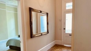 A hallway with a wooden herringbone floor, a mirror on the wall, and a door leading to another room. - Luxury Glasgow West End Apt.

 (Glasgow)