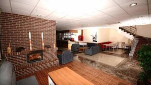 A spacious living area with a brick fireplace, comfortable seating, a kitchen in the background, and a staircase leading to an upper level. - Can Ilgaz Mountain Resort (Ilgaz)