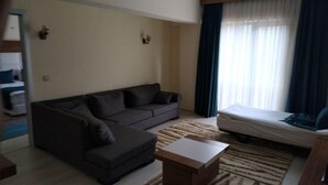 A living room with a sofa, a small table, a bed, and a window with curtains. - Can Ilgaz Mountain Resort (Ilgaz)