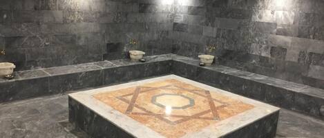A modern bathroom with dark marble walls, a central square with a geometric tile design, and two sinks with basins.
