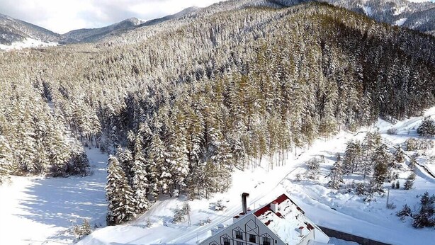 A snow-covered building with a symmetrical facade, surrounded by a forested area and mountains in the background. - Can Ilgaz Mountain Resort (Ilgaz)